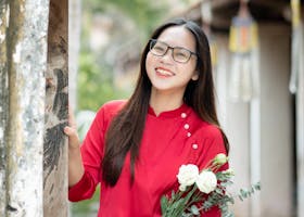 Portrait of a young woman in a red áo dài holding flowers in Hưng Yên, Việt Nam.
